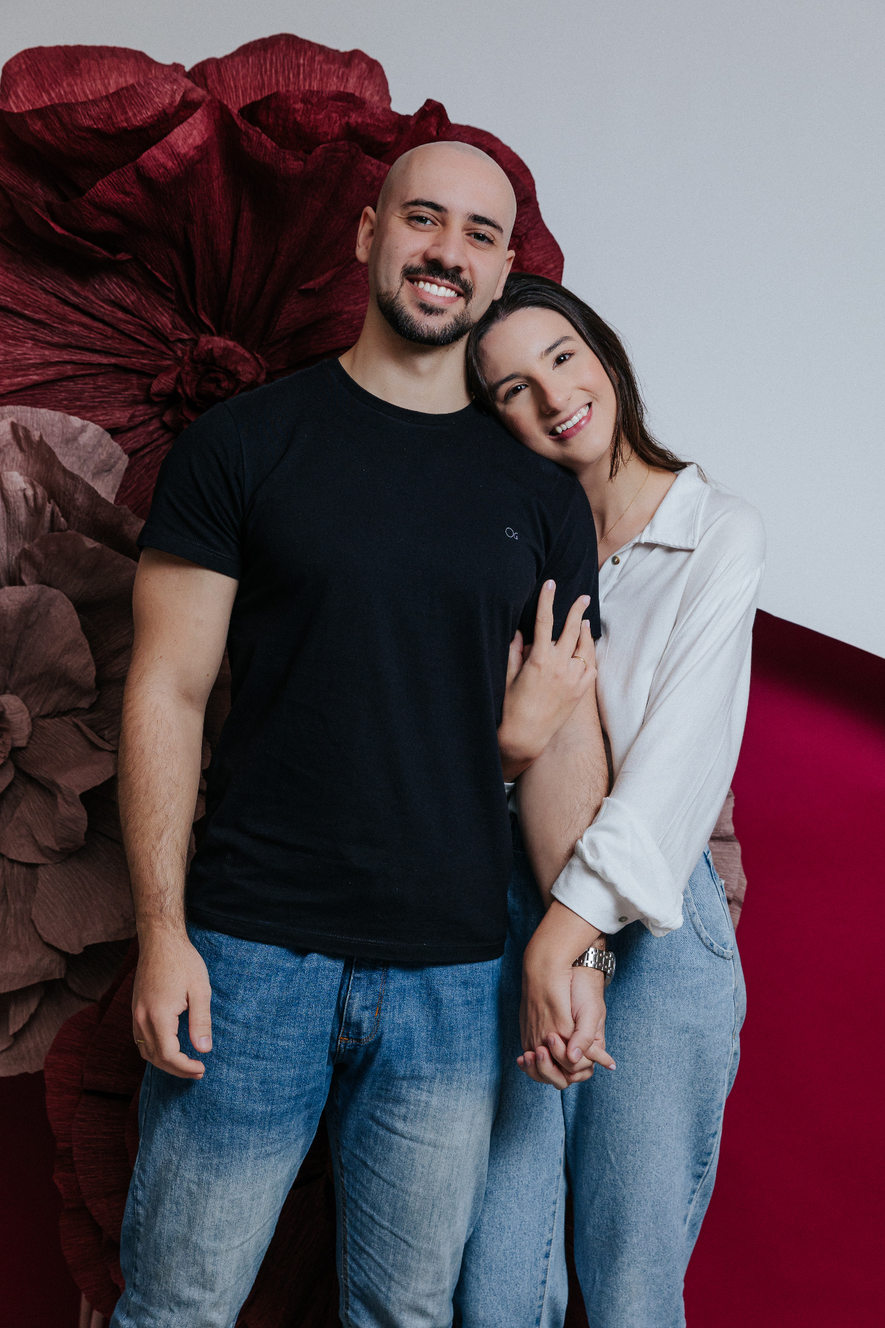 Casal abraçado em frente a flores de papel bordô